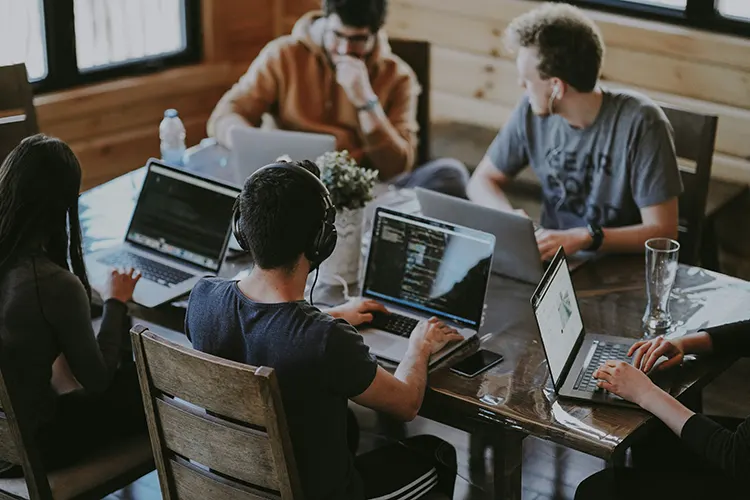 A collaborative software development team working together on laptops around a table.